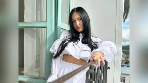 TessaWinsent — TessaWinsent with long black hair poses on a balcony wearing a white crop top and skirt.