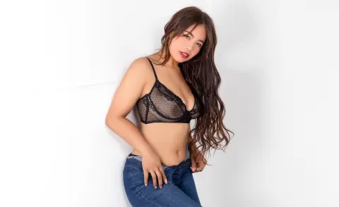 Young woman in black lace lingerie and blue jeans posing against a white background with a soft, natural mood.