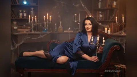 LaurenNewton — LaurenNewton reclines on a dark velvet chaise lounge wearing a blue satin robe with black lace trim.