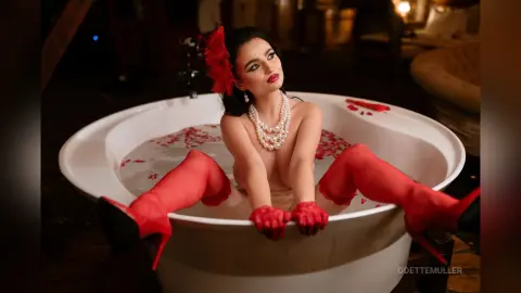 Glamorous woman in red gloves and stockings relaxing in a white bathtub filled with rose petals.