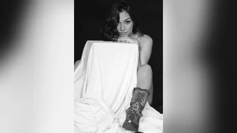 Moody black and white portrait of a young woman leaning on a white draped cloth in a dark studio setting.