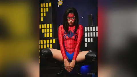 JessieLiu wears a red spider-themed bodysuit and black boots while sitting with her legs spread wide.