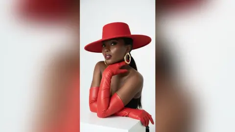 Elegant Black woman in a red wide-brimmed hat and matching red gloves posing against a white studio background.