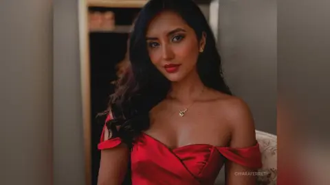 Elegant woman in a red off-the-shoulder satin dress posing with a glamorous mood in a warm indoor setting.