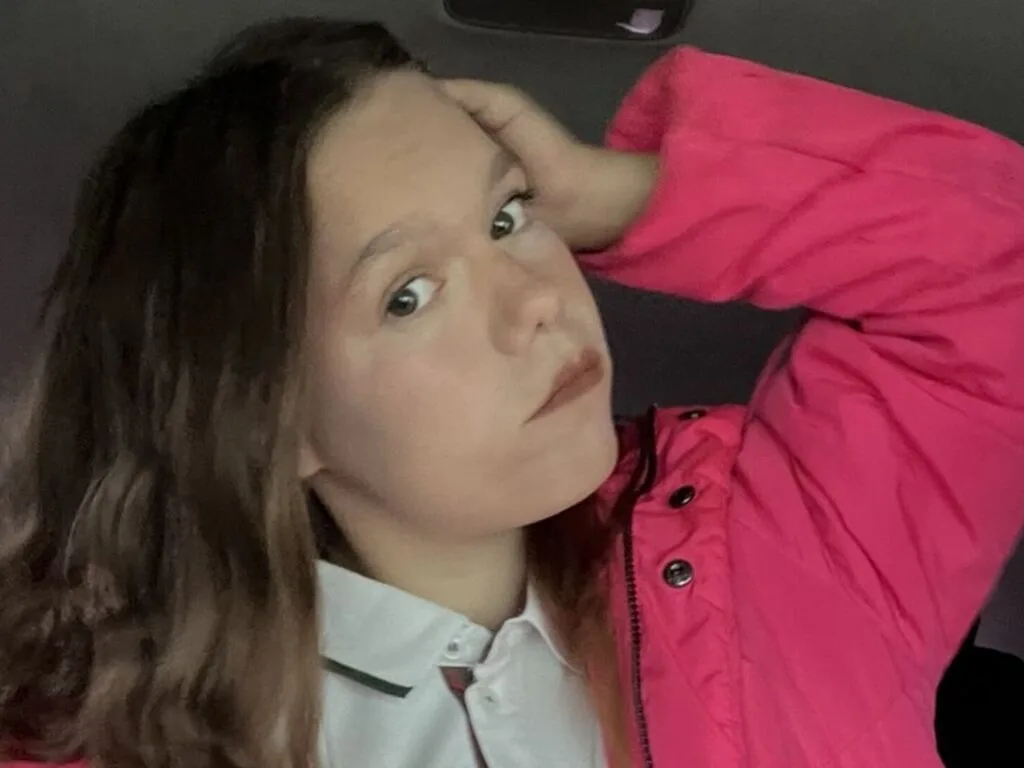 MozellKotlle poses in a bright pink puffer jacket with her hand resting in her long brown hair.