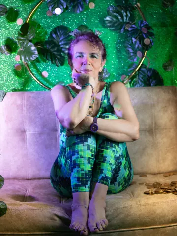 Woman in green patterned jumpsuit sitting on a beige sofa against a tropical leaf backdrop.