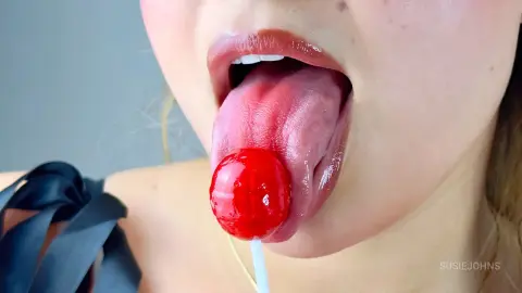 Close-up of a woman in a black outfit enjoying a bright red lollipop with a playful mood.
