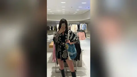 Stylish woman in a patterned black kimono and boots posing in a modern clothing boutique.