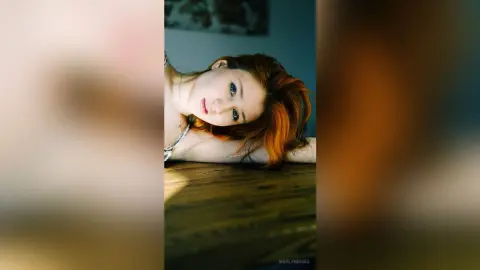 Redheaded woman in a silver necklace resting on a wooden surface with a dreamy, moody atmosphere.