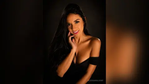 AlessaWaldorf smiles while posing in a black off-the-shoulder top against a dark background.