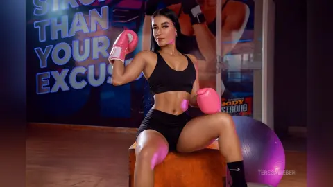 Athletic woman in black gym wear wearing pink boxing gloves sitting in a fitness studio with a confident mood.