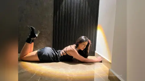 Fashionable woman in a black mini dress lying on a marble floor in warm, cinematic sunlight.