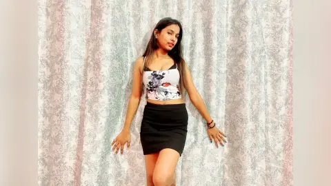 Young woman in a floral crop top and black mini skirt posing against a patterned curtain backdrop.