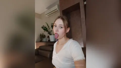Young woman in a white lace top making a playful expression in a modern living room setting.