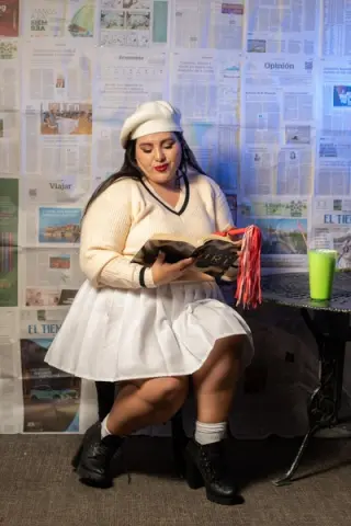 Woman in white sweater and beret reading a book against a newspaper backdrop in a cozy, studious mood.