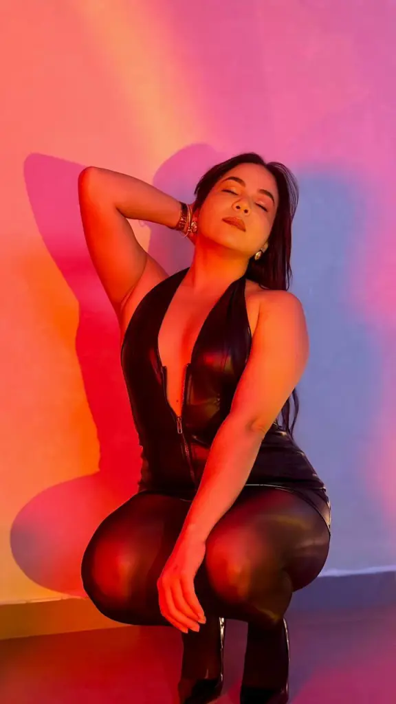 VictoriiaaCollins sits in a white chair wearing a dark green blazer against a bright green background.