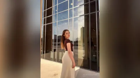 Stylish woman in a brown top and white trousers standing by a modern glass building in bright daylight.
