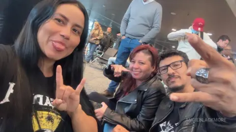 Three happy friends in casual outfits making hand gestures during a fun indoor gathering.