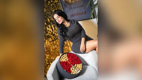 Elegant woman in a black sparkly dress sitting by a luxury gift box with red roses in a glamorous setting.