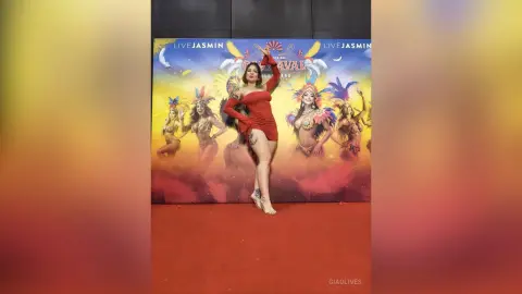 Woman in a red dress posing in front of a colorful carnival backdrop at a festive event.