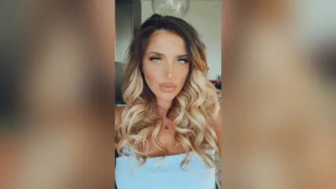 TiffanyAddams poses with long, wavy blonde and brown hair wearing a light blue top.