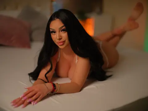 Young woman with long dark hair in white lingerie relaxing on a bed in a cozy, warm bedroom setting.