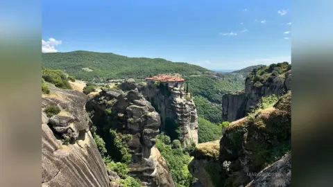 Panoramic view of the historic Meteora monasteries perched atop massive rock formations in a lush Greek landscape.