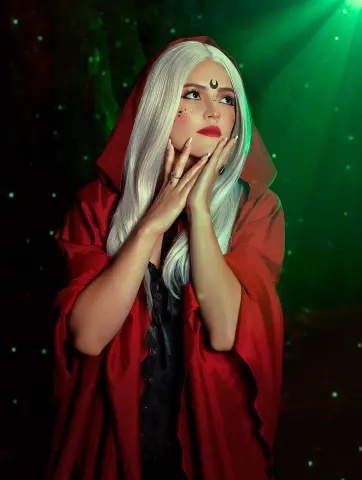 AlicceGray wears a red hooded cloak over a black lace top, framing her long white hair and red lips while she poses with her hands against her face.