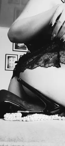 Elegant woman in black lace lingerie and high heels posing in a moody black and white indoor setting.