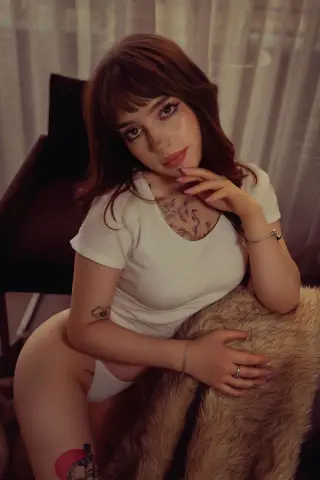 Brunette woman in a white t-shirt sitting on a fuzzy chair with a dreamy, soft-lit aesthetic.
