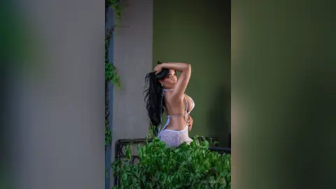 DayanaHille poses outdoors in white lace lingerie, running her hands through her long dark hair while looking back over her shoulder.