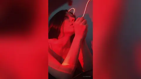 Young woman in a black tank top looking up under moody red neon lighting in a dark room.