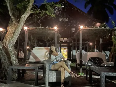 Woman in a white tie-front top and denim shorts relaxing in a lounge chair at a tropical night resort.