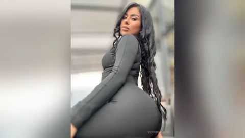 Curvy woman in a sleek black long-sleeve dress posing confidently in a bright, modern indoor setting.