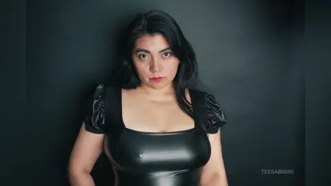 Woman in a black puff-sleeve bodysuit posing against a dark moody background.