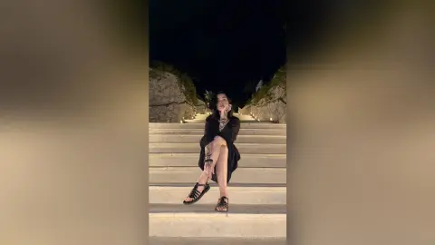 Young woman in a black outfit sitting on outdoor stone stairs at night under moody lighting.
