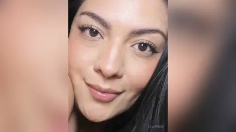 Close-up portrait of a smiling young woman with long dark hair and natural makeup looking into the camera.