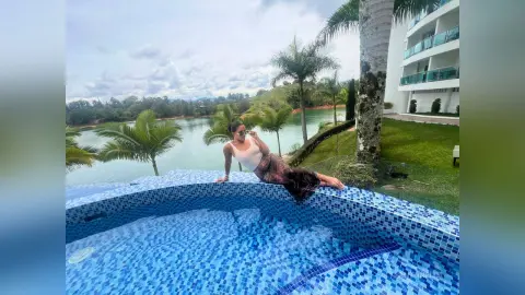 Woman in a white tank top relaxing by a luxury resort pool overlooking a tropical lake and palm trees.