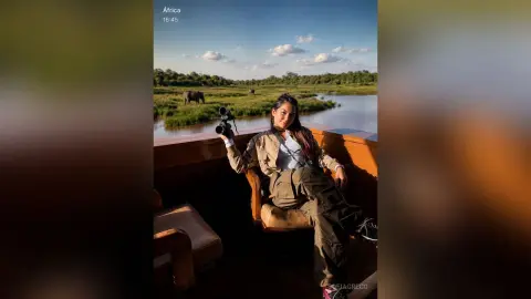 SofiaGreco sits on a wooden chair wearing olive green cargo pants and a light tan jacket against a river landscape.
