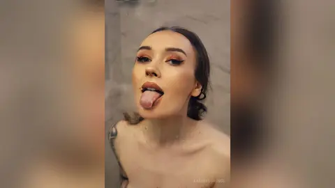 Young woman with winged eyeliner sticking her tongue out in a playful mood against a neutral background.