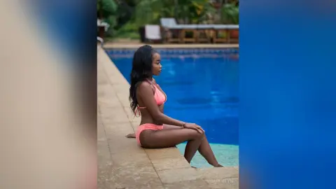Young woman in a peach bikini relaxing by a tropical swimming pool on a sunny summer day.