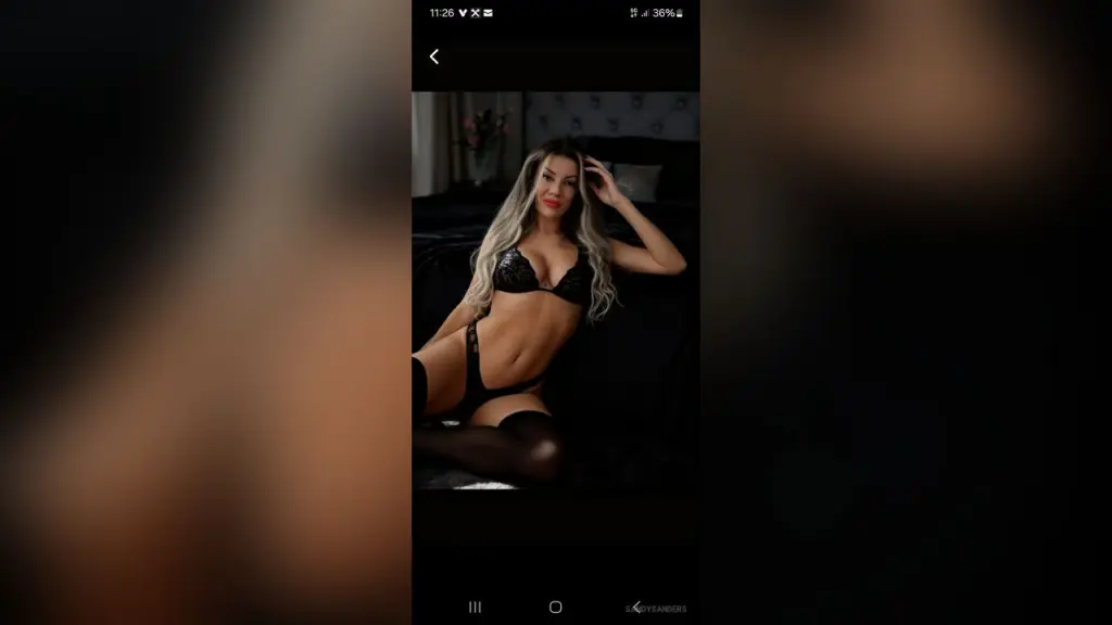 SandySanders — SandySanders reclines on a black bed wearing a black lace bra and matching black lace thong or g-string.