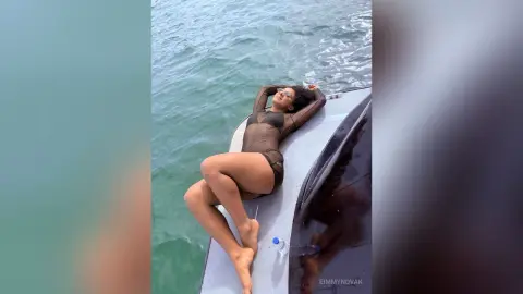 Relaxed woman in a brown bodysuit sunbathing on a boat in the turquoise ocean water.