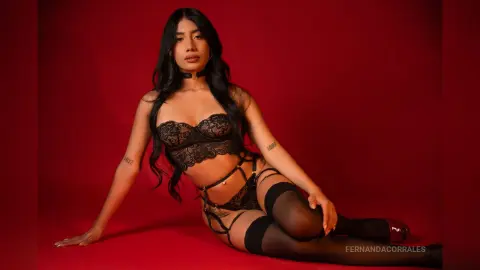 Young woman in black lace lingerie and stockings posing against a bold red background with a moody aesthetic.