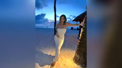Woman in a white strapless dress posing on a tropical beach at dusk under a blue twilight sky.