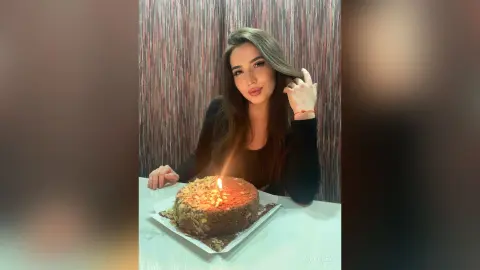 Young woman in a black top celebrating her birthday with a lit chocolate cake in a cozy indoor setting.