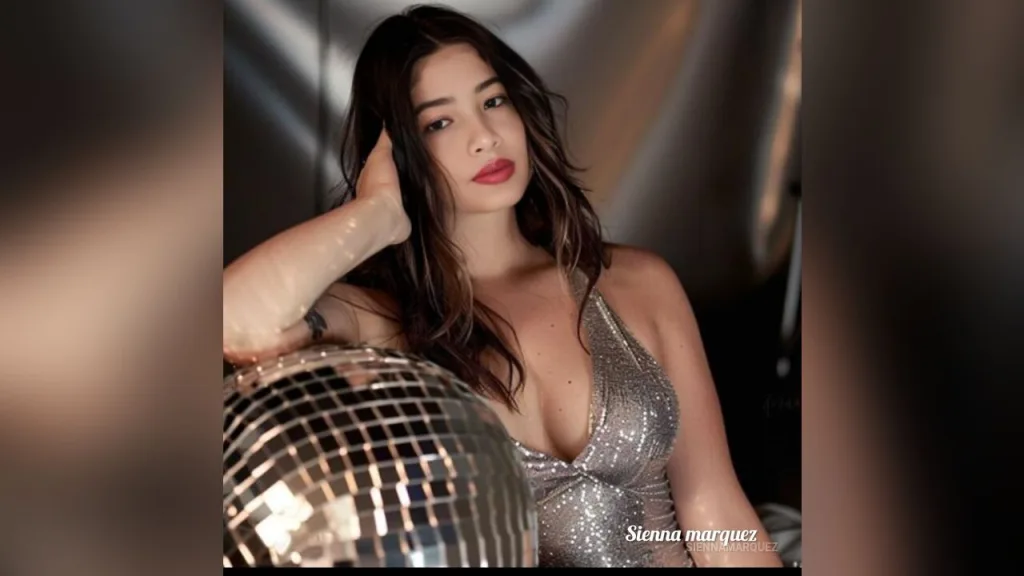 SiennaMarquez — SiennaMarquez poses in a silver sequin dress next to a disco ball.