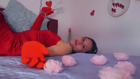 Woman in red outfit lying on bed with pink flowers for a romantic Valentine's Day mood.