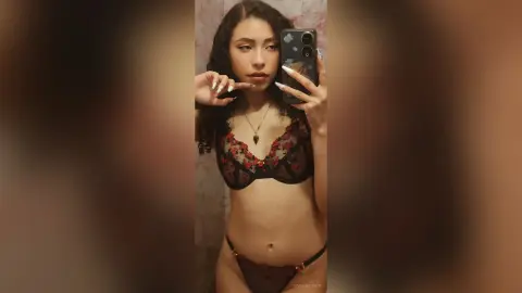 Young woman with curly hair in black lace lingerie posing for a moody mirror selfie in a dimly lit room.