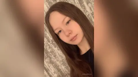 Young woman with long brown hair wearing a black top in a cozy indoor setting with a soft, natural mood.